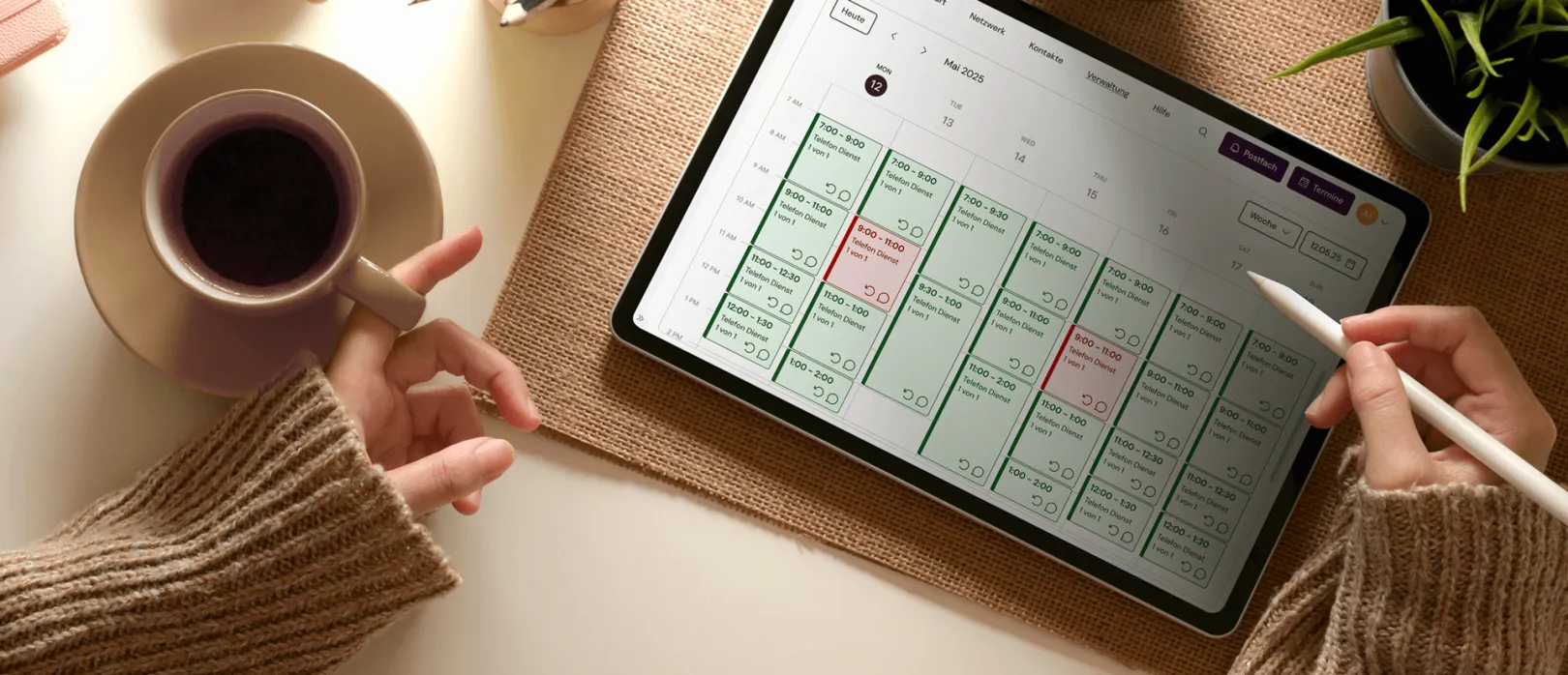 Desktop with a tablet on it with which a person is interacting. The display shows a calendar and the person is holding a cup of coffee and a tablet pencil in the hands.