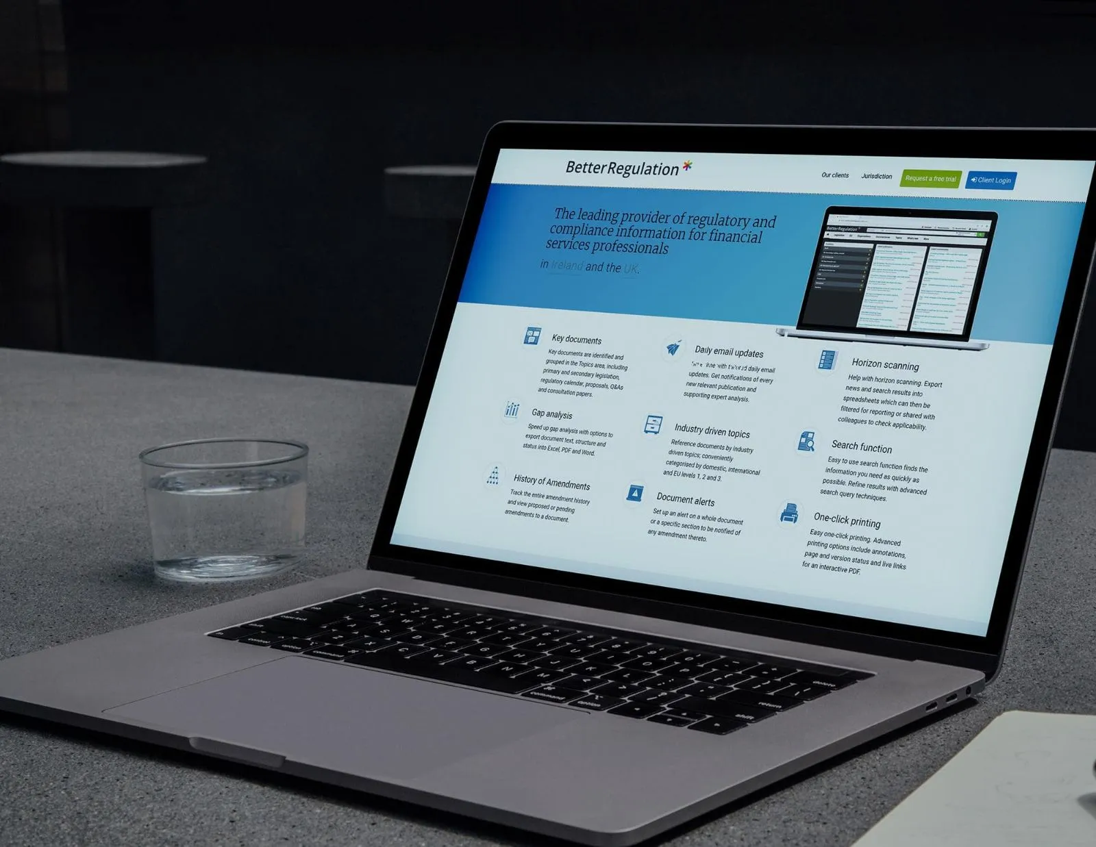 A laptop on a desk displaying the BetterRegulation.com homepage with the regulatory compliance hero banner and feature grid for financial services professionals in Ireland and the UK.