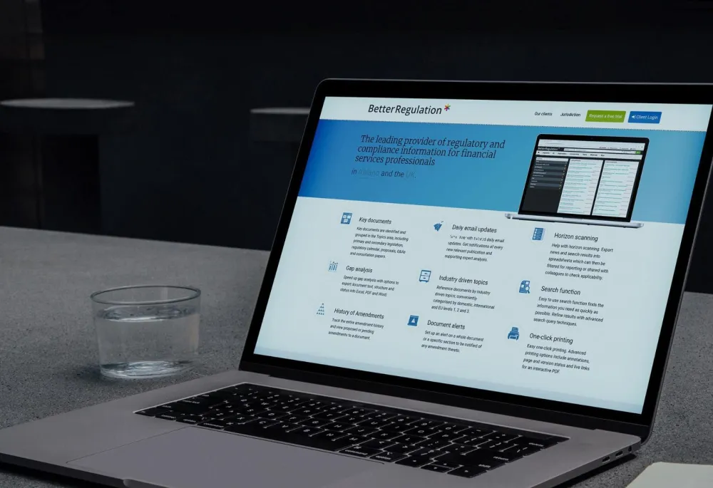 A laptop on a desk displaying the BetterRegulation.com homepage with the regulatory compliance hero banner and feature grid for financial services professionals in Ireland and the UK.