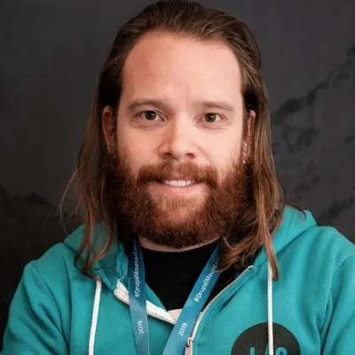A man with long ginger hair and a ginger beard in a teal hoodie.