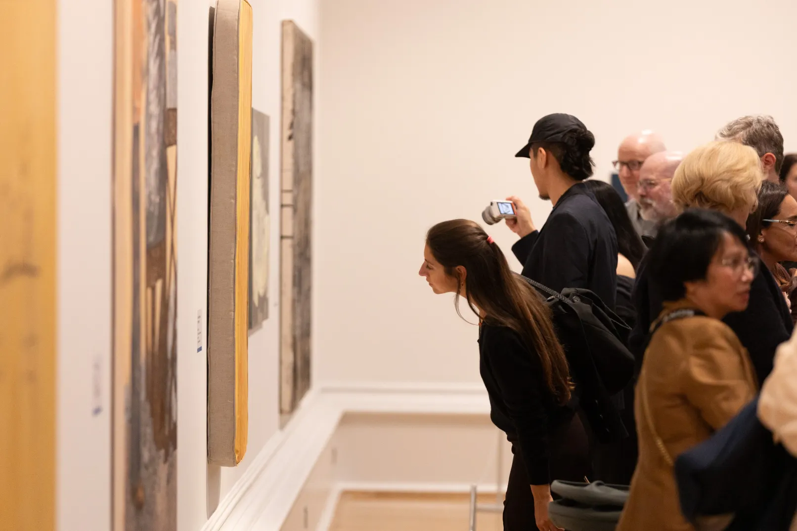 Visitors looking closely at paintings displayed along a gallery wall