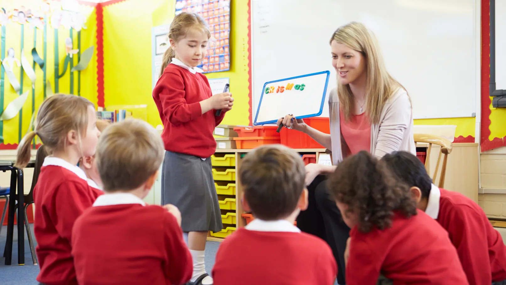 Teacher holding a small whiteboard while working with children in red school uniforms