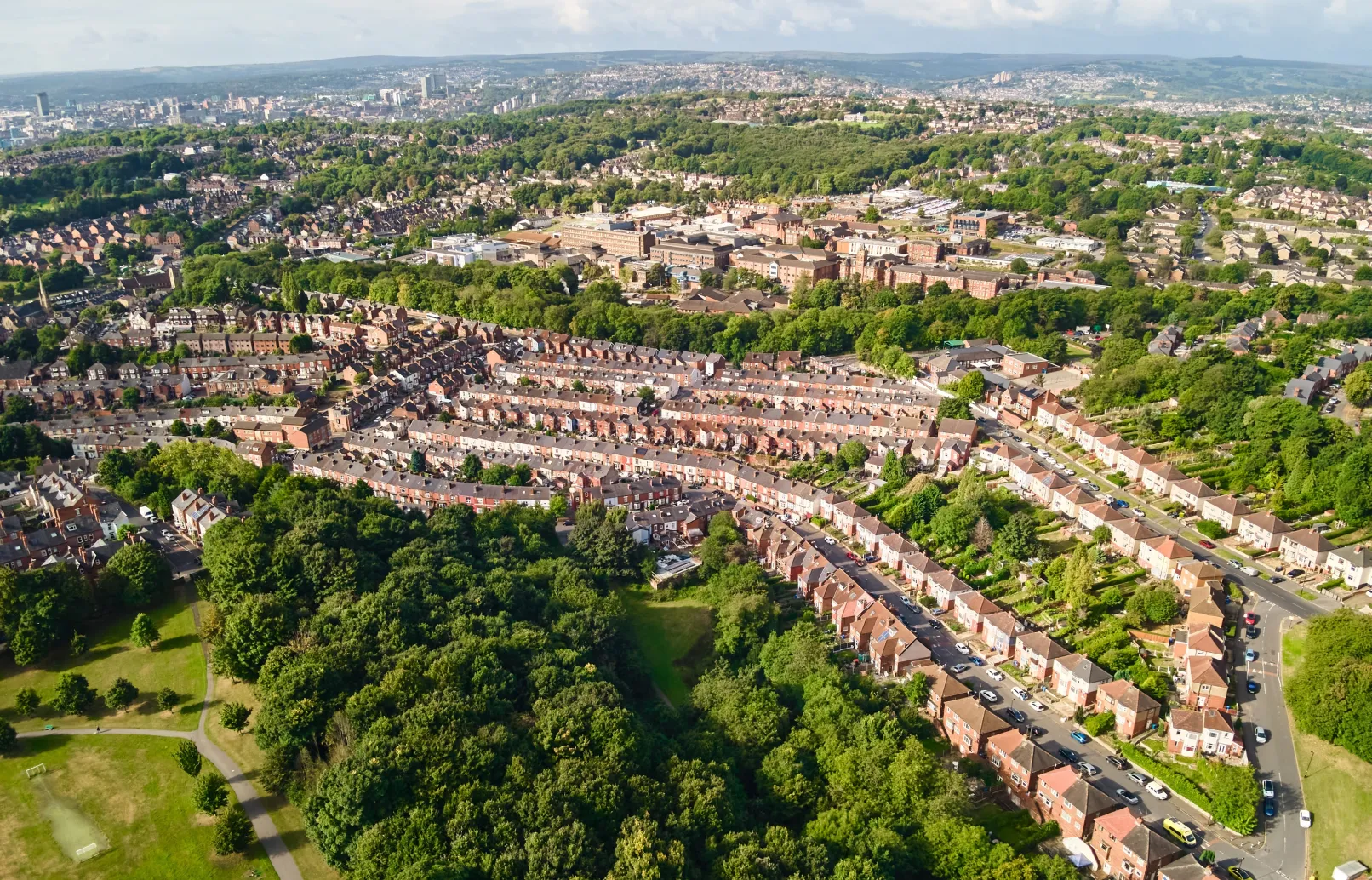 Aerial view across Sheffield, with terraced neighbourhoods, green spaces and the city skyline in the distance