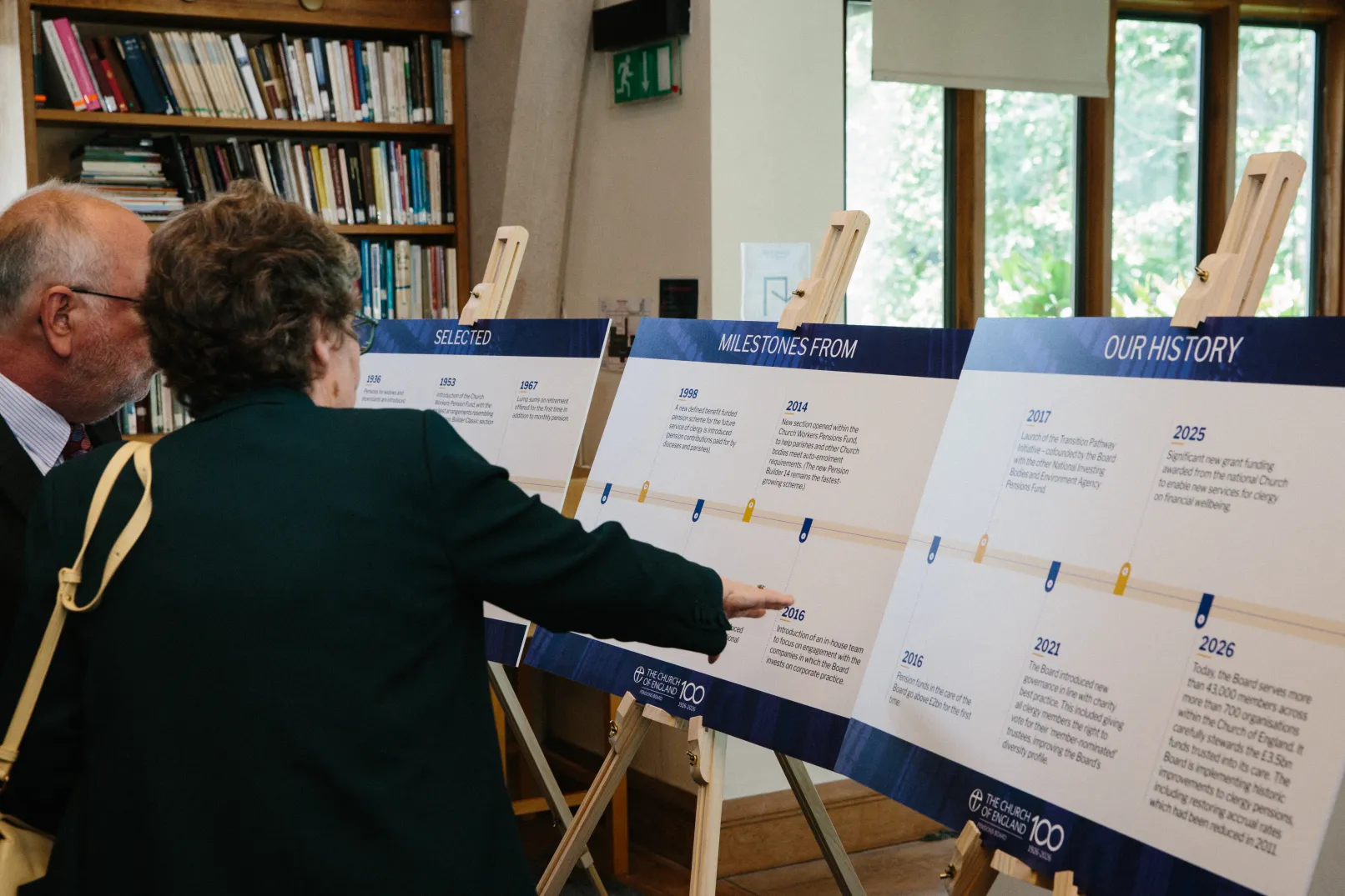Two guests examining display boards charting the history of the Church of England Pensions Board