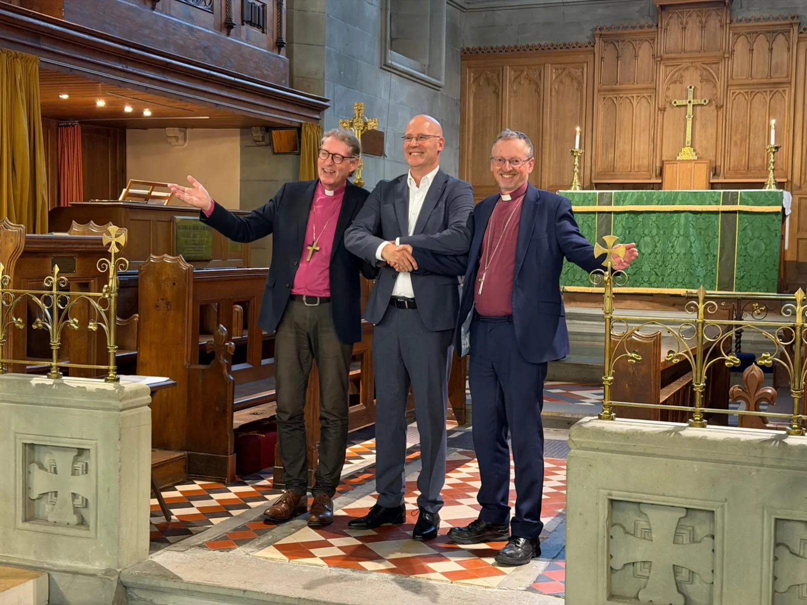 Two bishops and a fellow visitor standing together in front of a church altar
