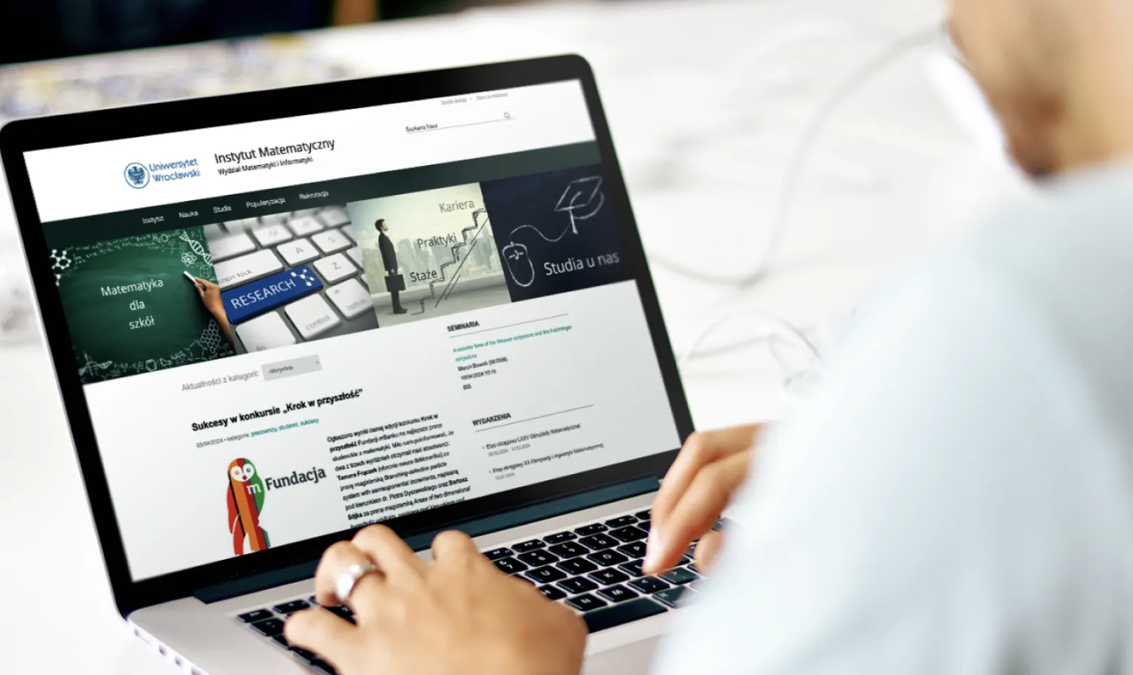 Person using a laptop displaying the Institute of Mathematics at the University of Wroclaw Drupal website homepage with navigation and featured academic content tiles.