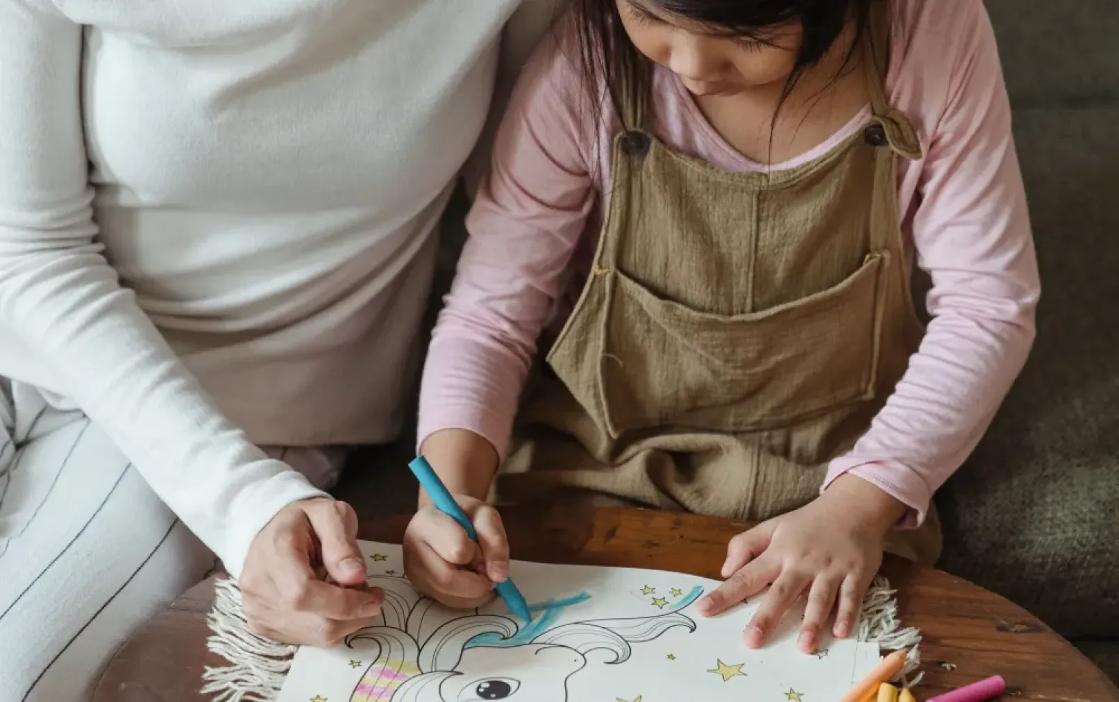 young girl drawing while supported by her parent sitting behind her