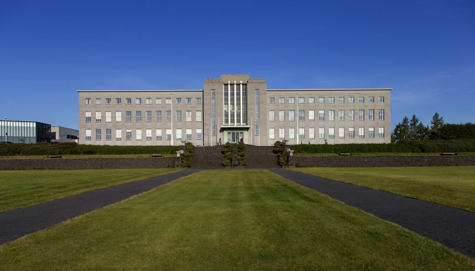 A large concrete building in the background with grass lawns in front. 